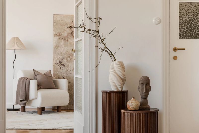 View through open doors onto a serene lounge with soft armchair, textured art, and calm, natural styling. Home decor.