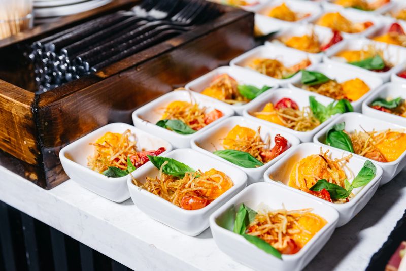 Vibrant mini appetizers served in white bowls, featuring fresh tomatoes, crispy potato garnish, and basil leaves for elegant catering.