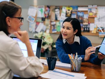 Two women discussing work at a desk.