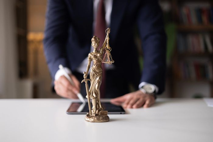 Lady Justice statue in focus with blurred businessman in background.