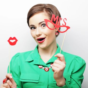 Woman in green holding red photo booth props, playful expression.