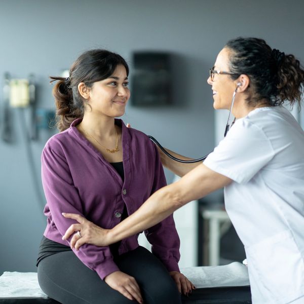 Doctor using stethoscope to check patient's heart in clinic.