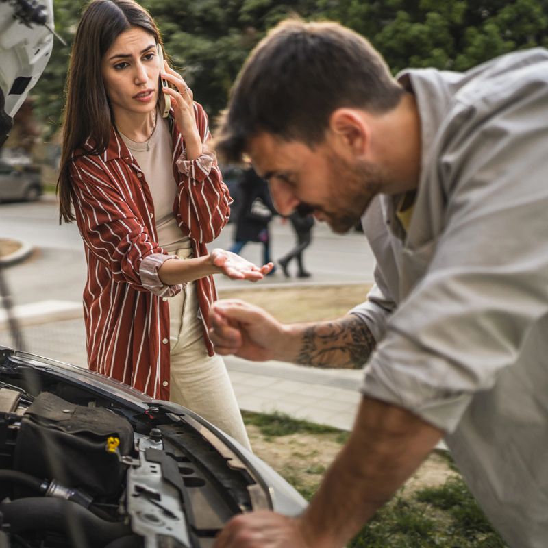 Boyfriend check car engine while girlfriend calls for assistance