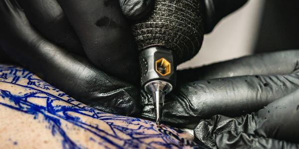 Close-up of a tattoo artist working with a tattoo machine on a blue stencil.