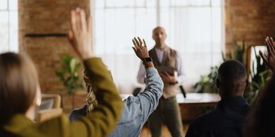 People raising hands in a meeting or classroom.