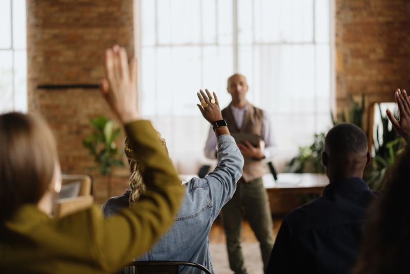 Audience raising hands to ask questions during a business conference with a mature adult speaker