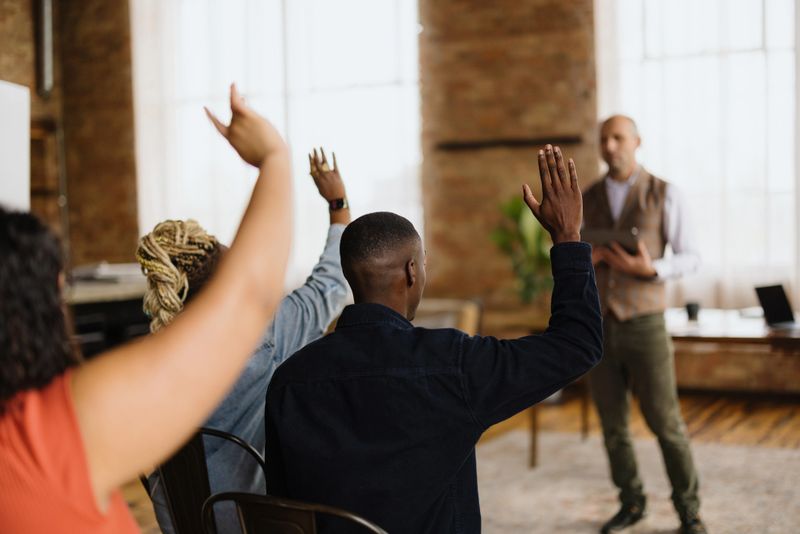 Students raising hands to ask questions during a lesson, engaging with their teacher in a lively classroom discussion