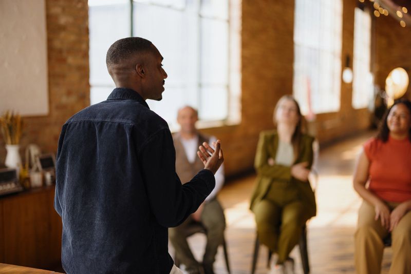 Young businessman leading a meeting in a modern office and speaking to his colleagues sitting on chairs
