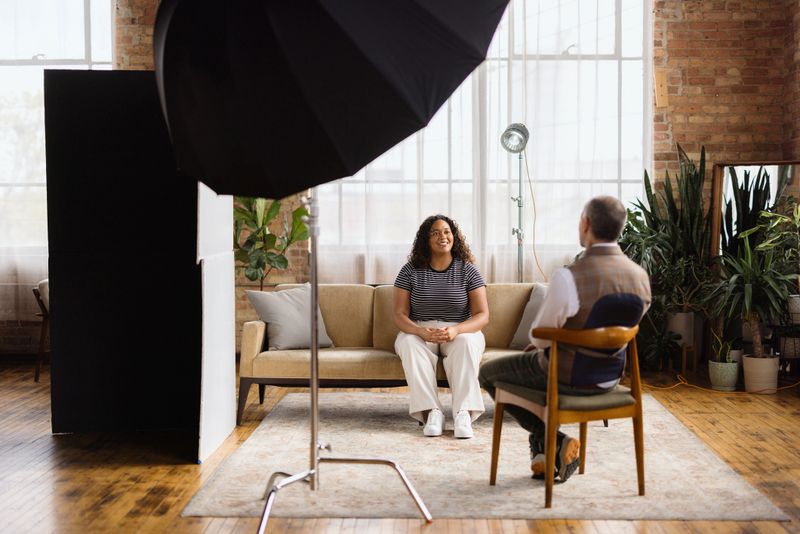 Young woman sitting on a couch in a modern loft studio, engaging in an interview with a journalist, exchanging thoughts and ideas