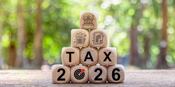 Wooden blocks spelling TAX 2026 with financial icons on top, set against a blurred green background.