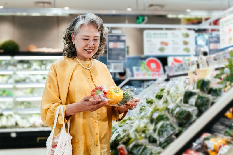 Elegant Asian senior woman shopping for vegetables in supermarket.