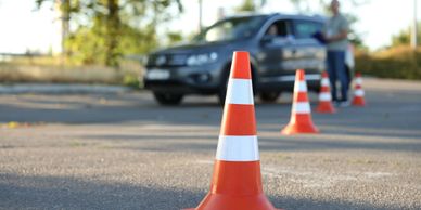 Traffic cones lined up on a road with a car and person in the background.
