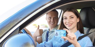Woman holding driver's license in car, man giving thumbs up.