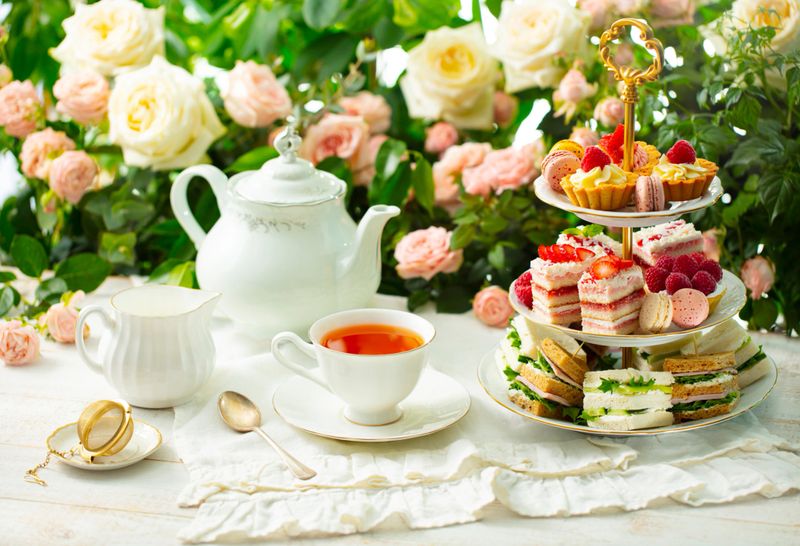 Afternoon tea table. Assortment of cakes, sweets and sandwiches. Rose garden background.