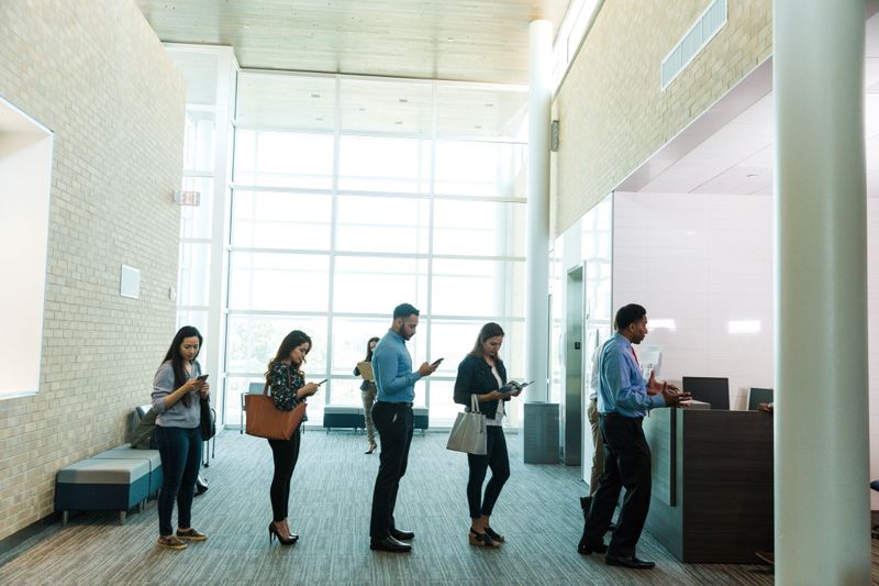 Multiracial people using smartphones and tablets while waiting indoors.