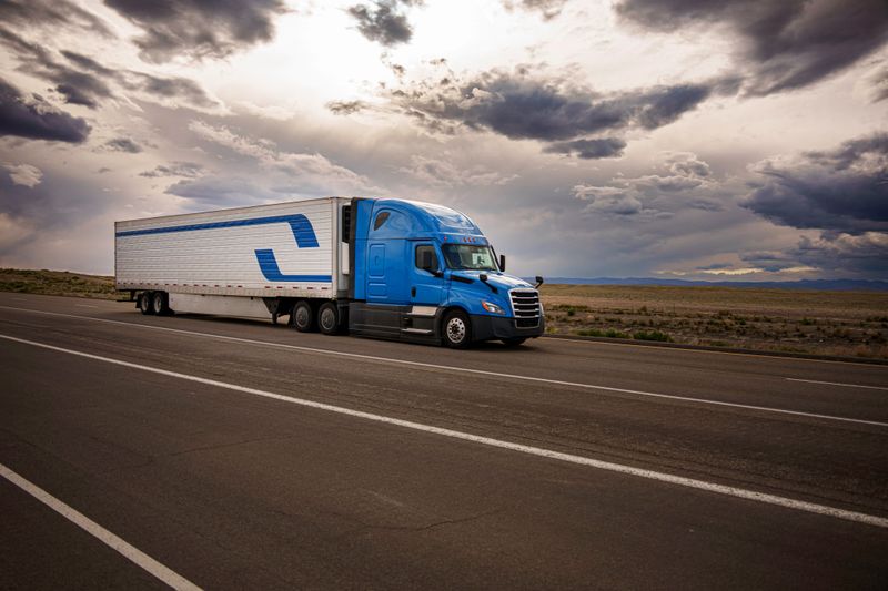 Side View Blue Semi-Trailer Long Haul Tractor Truck Speeding Down a Four Lane Highway in Eastern Utah Desert