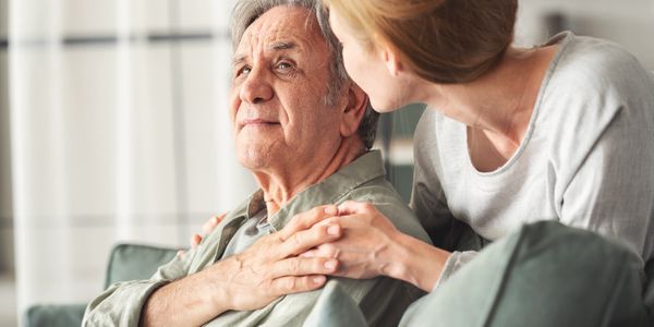 A woman comforting an elderly man by holding his shoulder with care and concern.