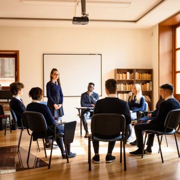 Group meeting in a classroom with one person speaking.
