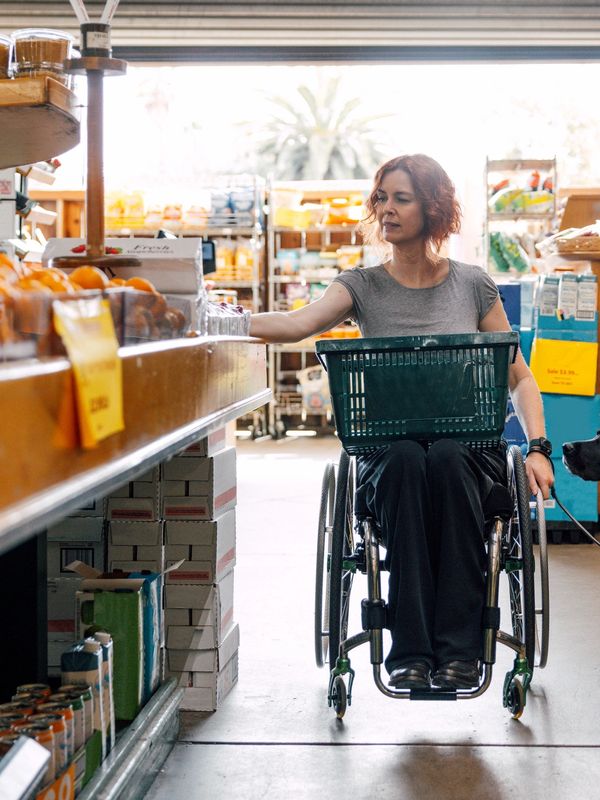 A woman in a wheelchair shopping for produce at a grocery store.