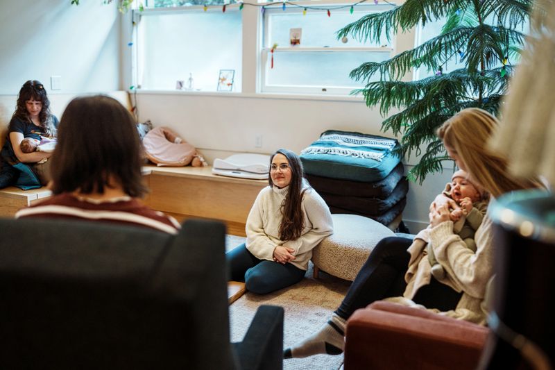 A female physical therapist and certified lactation consultant listens with empathy and encouragement as attendees of a postpartum support group she leads share concerns, ask questions, and offer advice.
