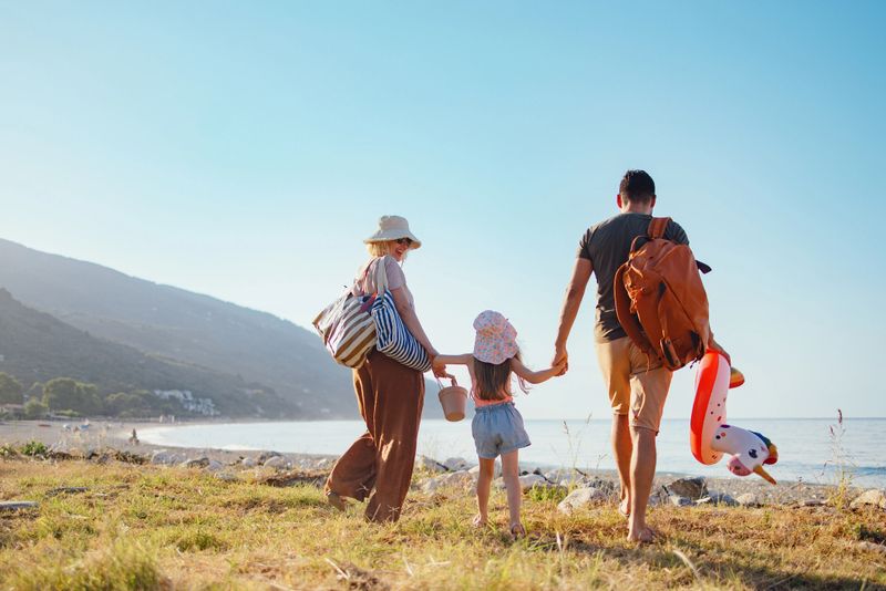 A family enjoys a sunny summer day, walking towards the beach with scenic surroundings.