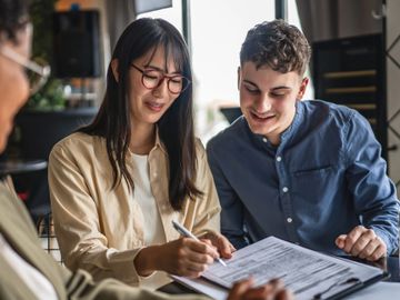 Young couple signing documents with a professional in a bright office.