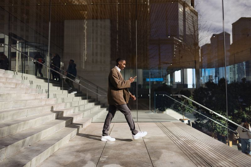 Young businessman walking and using smartphone in front of modern glass building