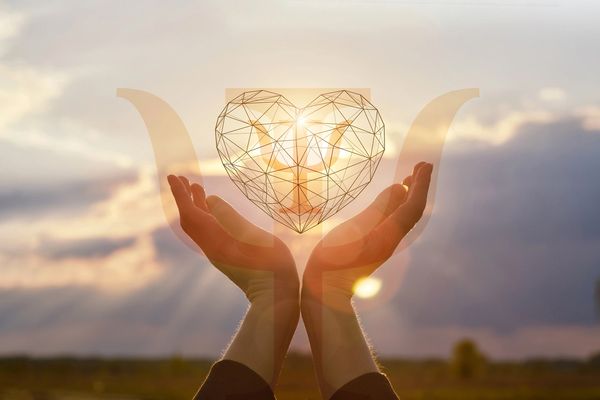 Hands holding a glowing wireframe heart with a psychology symbol at sunset.