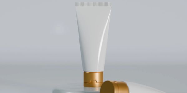 Minimalist cream tube with gold cap on a smooth surface.