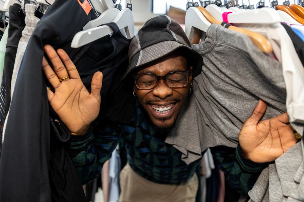 Man happily peeking through clothes on hangers.