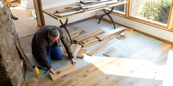 Man installing wooden floor panels in a room.