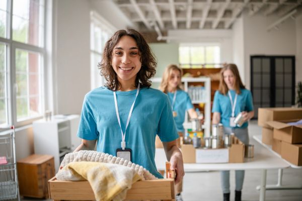 Woman kneeling beside boxes filled with household supplies and groceries indoors.