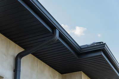 Modern roof corner with gutter and downspout under blue sky.