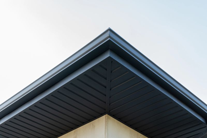 The sleek lines of a modern roof reveal sharp angles and a minimalist design, set against a clear blue sky highlighting architectural elegance.