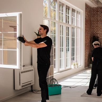 Three people cleaning a bright, modern living room with large windows.