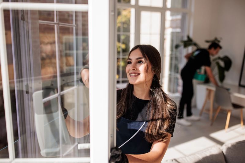 Focused female cleaner using high-performance equipment to wash windows inside a contemporary apartment.
