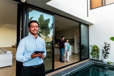 Real estate agent smiling near a modern house pool with clients inside.