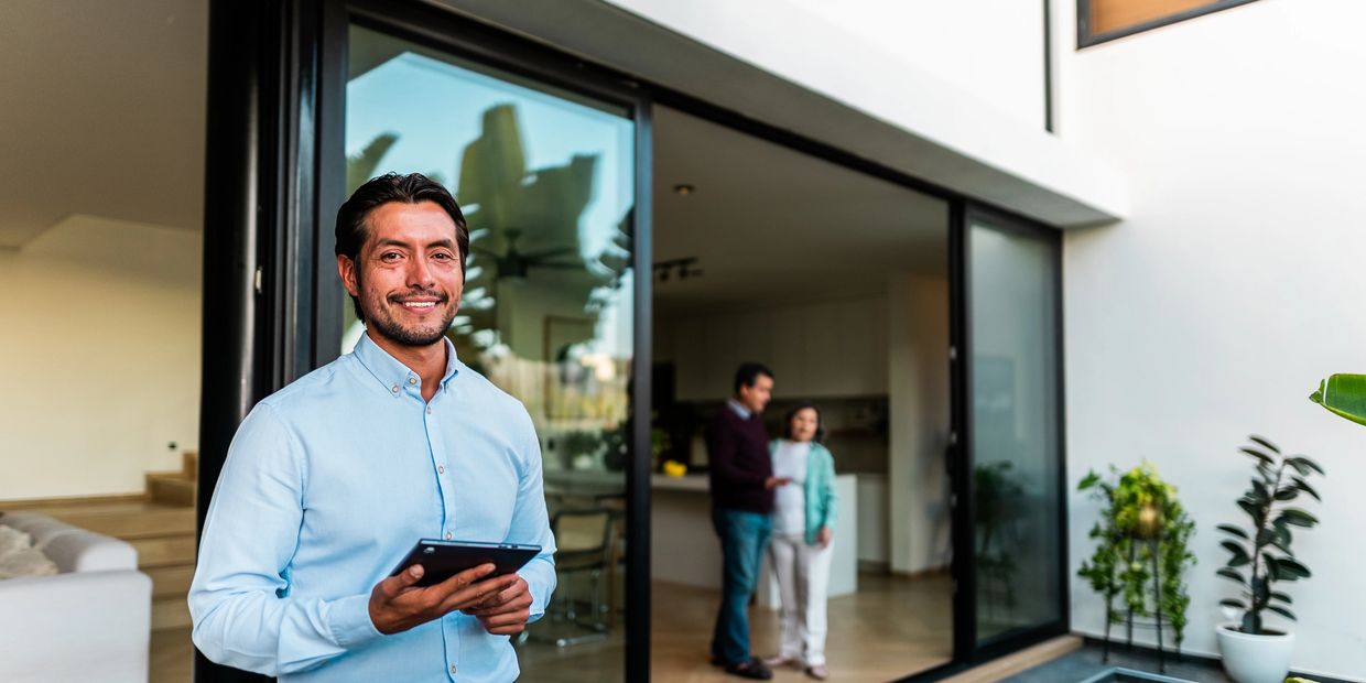 Smiling real estate agent standing by a modern home with a pool, holding a tablet.