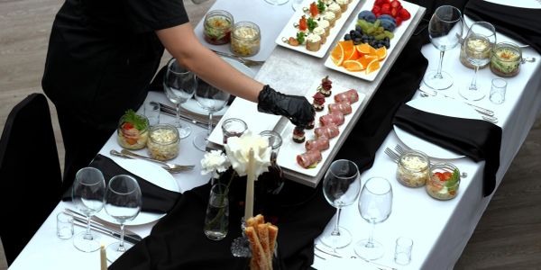 Person setting appetizers on a dining table with black and white decor.
