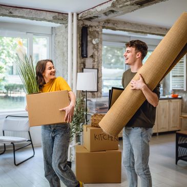 Young couple happily moving into a new home with boxes and rolled carpet.