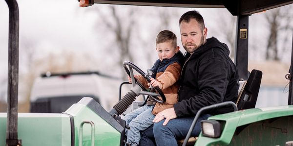 A father and son sitting on a green tractor together.
