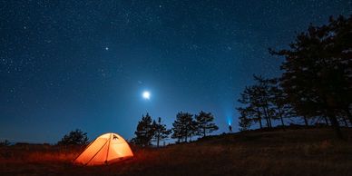 Glowing orange tent under a starry night sky with the moon shining.