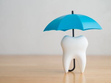 A tooth figurine protected by a blue umbrella symbolizing dental care.