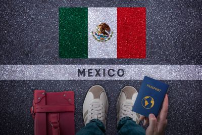 Travel essentials including a passport and bag near a painted Mexican flag.