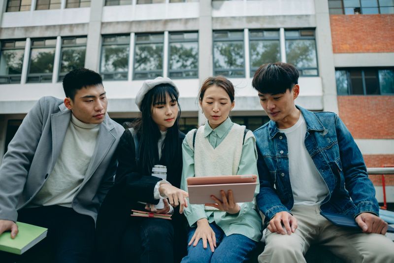Four Asian university students walk across campus, engaged in an animated discussion about their coursework. The scene highlights the collaborative spirit of higher education and the importance of peer learning in today’s academic environment. Amid rising tuition costs and debates on access and equity, their interaction symbolizes gender-inclusive teamwork and shared academic resilience. As remote and hybrid learning becomes increasingly common, these in-person exchanges underscore the value of face-to-face communication in building intellectual and emotional support.