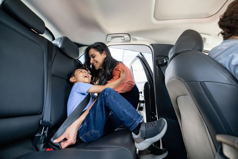 Happy Latin American mother helping her son to fasten his seat belt in a car â safety concepts