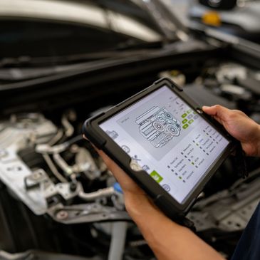 Mechanic using a tablet to diagnose a car engine with hood open.