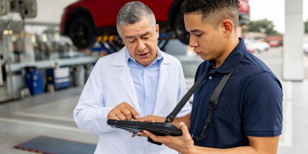 Dos hombres revisan información en una tablet en un taller mecánico.
