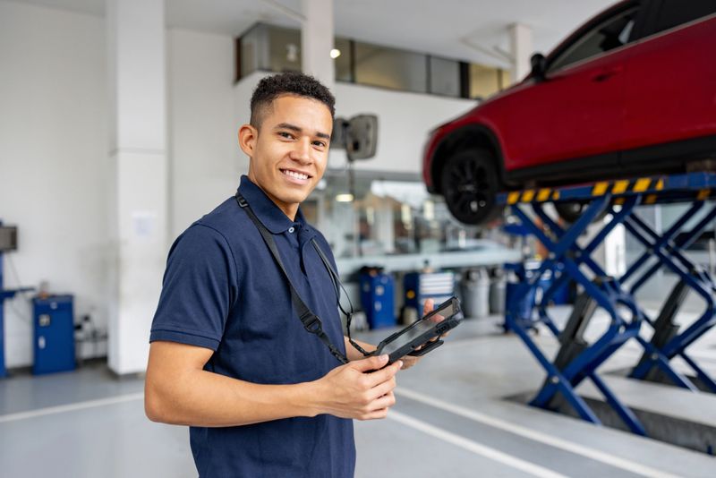 Portrait of a Latin American mechanic working at a car garage and holding a digital tablet while looking at the camera