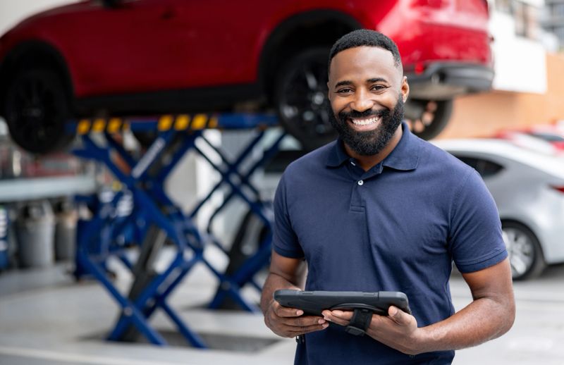 Portrait of an African American mechanic working at a car garage and holding a digital tablet while looking at the camera